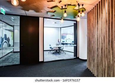 Interior Photography Of A Modern Office Front Entrance With Decorative Timber Feature And Pendant Lighting, A Meeting Room With A Male Employee And Open Plan Office In The Background