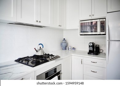 Interior Photography Of A Modern White Kitchen With Marble Bench Top, Stainless Steel Appliances, Kettle And Decorative Items