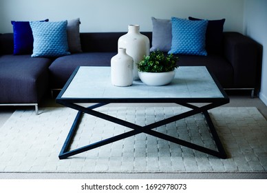 Interior Photography Of A Simple Modern Lounge Room With A Dark Blue Modular Sofa With Cushions, A Stone Topped Coffee Table With Decorative Bottles & A Succulent Plant, Shot Front On