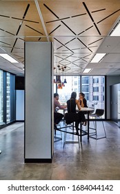 Interior Photography Of Staff Holding A Meeting In A Modern Office Breakout Area With Lunch Table And Stools, Laser Cut Wooden Ceiling, Pendant Lighting, Polished Concrete Floors And City Views