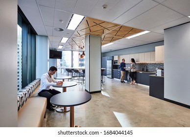 Interior Photography Of Staff In A Modern Office Breakout Area With Kitchen, A Lunch Table And Stools, A Decorative Laser Cut Wooden Ceiling, Pendant Lighting, Polished Concrete Floors And City Views