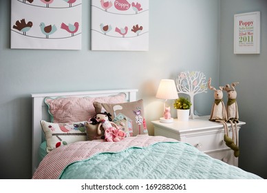 Interior Photography Of A Stylish Little Girl's Bedroom With Aqua And Pink Bedding, Decorative Cushions, Side Table With Lamp, Wall Art And Toys