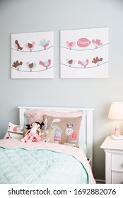 Interior Photography Of A Stylish Little Girl's Bedroom With An Aqua And Pink Bedding, Decorative Cushions, Side Table With Lamp, Wall Art And Toys