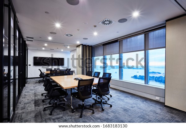 Interior photography of two large modern corporate\
board rooms divided by a concertina wall with neutral tones, large\
beech timber meeting tables, black chairs, glass walls and harbour\
views