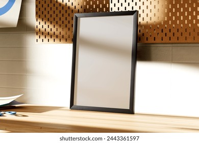 Interior poster mock up with A3 empty frame standing on work desk, in room with white wall and pegboard. Sunlight through the windows. Side view. 3D rendering
