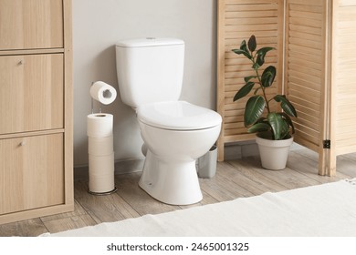 Interior of restroom with toilet bowl, plant and paper holder near grey wall