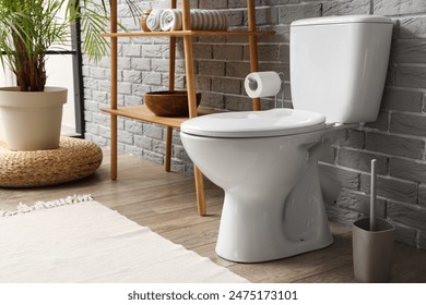 Interior of restroom with toilet bowl, plant and shelving unit near grey brick wall