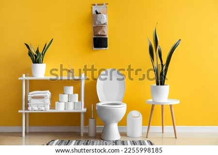 Interior of restroom with toilet bowl, shelving unit and houseplants