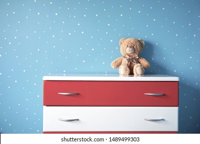 The Interior Of The Room With A Blue Star Wall And One White Red Chest Of Drawers. Teddy Bear In Nursery. 