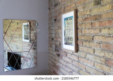 Interior Of A Room With Exposed Brick Wall And Mirror Reflecting Picture And Light Bulb Hanging On The Wall