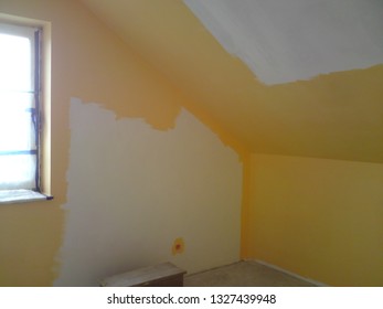An interior of a room under construction, walls covered with a primer paint and then partially painted in orange color, the concrete floor and the window