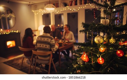 Interior Shot Of Warm Cozy Christmas Decorated Family Home. Family Sitting At Dinner Table Having A Christmas Eve Dinner Together.