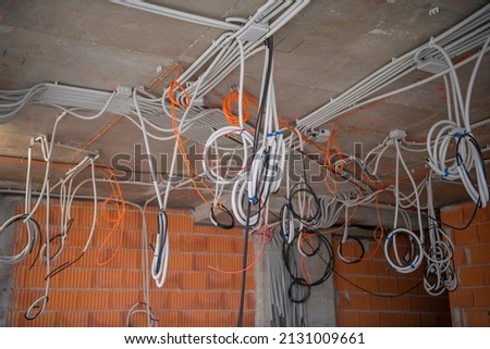 interior of skyscraper floor under construction. Cables, pipes and tubes hanging from ceiling of room. Building under construction, work in progress. Placement of electrical wires and cables.