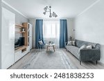 The interior of a small living room in European style apartment . The living room has a wardrobe for storing things , a TV , a coffee table , sofa and an armchair .