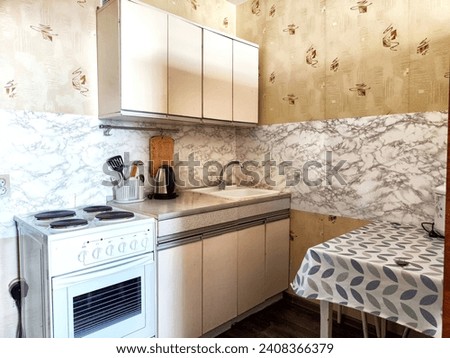 The interior is small old kitchen with a table, stool, cabinets, sink and stove. Design in the Soviet poor outdated style