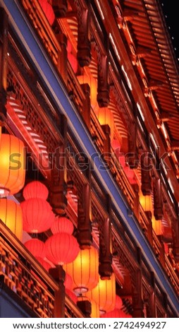 An interior space with a ceiling adorned with hanging red lanterns and illuminated with warm, orange toned lights