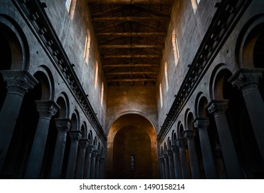 The interior with stone columns and Corinthian capitals and the ceiling with wooden beams of an ancient church or medieval cathedral, with colonnade and arches and apse in the background - Powered by Shutterstock