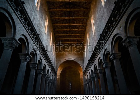 The interior with stone columns and Corinthian capitals and the ceiling with wooden beams of an ancient church or medieval cathedral, with colonnade and arches and apse in the background