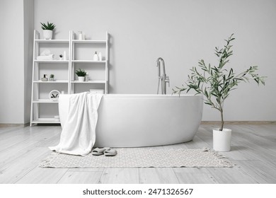 Interior of stylish bathroom with bathtub, shelving unit and olive tree - Powered by Shutterstock