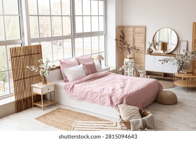 Interior of stylish bedroom with bed, commode and vases of blooming tree branches near window