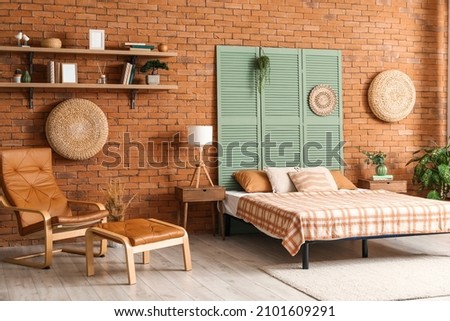 Interior of stylish bedroom with folding screen near brick wall