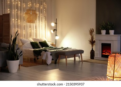 Interior of stylish bedroom with modern lamp, houseplants and fireplace in evening - Shutterstock ID 2150395937
