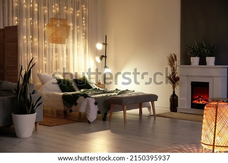 Interior of stylish bedroom with modern lamp, houseplants and fireplace in evening