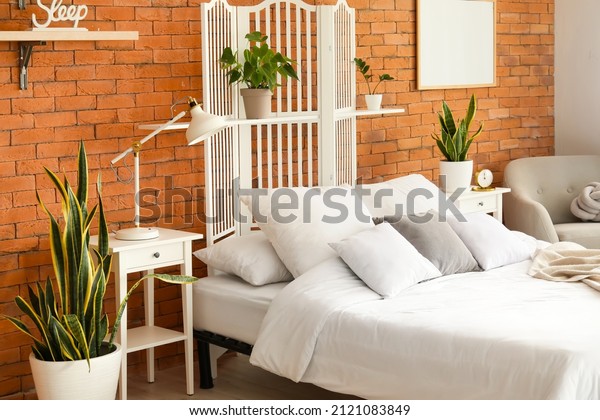 Interior of stylish bedroom with white\
folding screen and\
houseplants