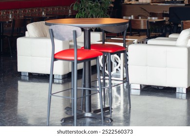 The interior of a stylish dining area of an upscale restaurant. There's two red leather pub chrome chairs with a round table, white leather couches, wooden chairs and tables. The lounge is elegant.