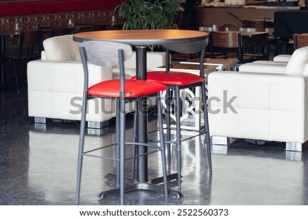 The interior of a stylish dining area of an upscale restaurant. There's two red leather pub chrome chairs with a round table, white leather couches, wooden chairs and tables. The lounge is elegant.