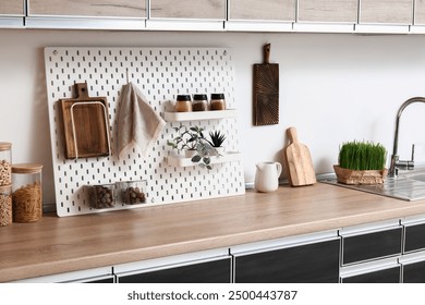 Interior of stylish kitchen with black counters, peg boards and white wall