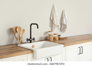 Interior of stylish kitchen with white counters, utensils and sink