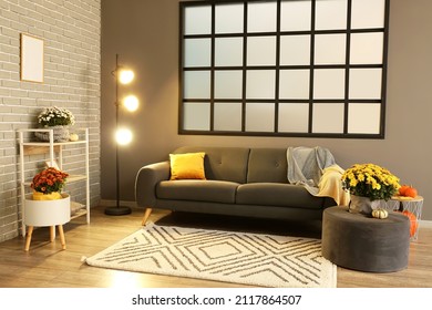 Interior of stylish living room with comfortable sofa, glowing floor lamp and Chrysanthemum flowers - Shutterstock ID 2117864507