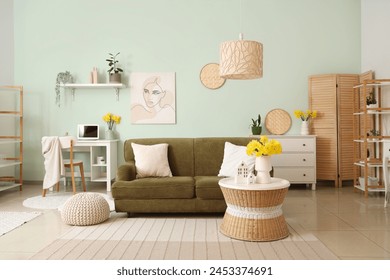Interior of stylish living room with comfortable sofa, chest of drawers, coffee table and vase of narcissus flowers