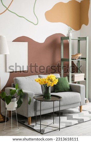 Interior of stylish living room with cozy grey sofa and blooming narcissus flowers on coffee table