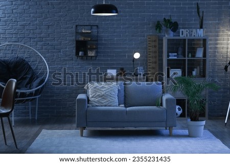 Interior of stylish living room with sofa and shelving unit at night