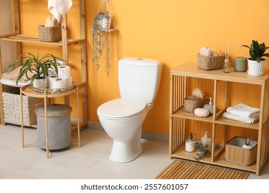 Interior del baño con estilo con tazón de inodoro blanco, mesa de centro y estantería cerca de la pared naranja