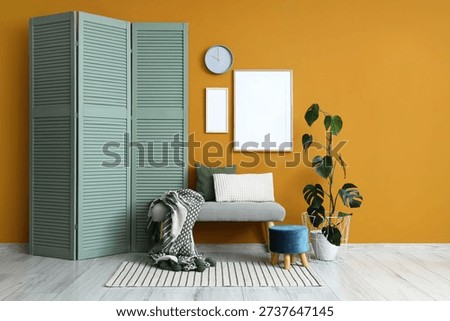 Interior of stylish room with clock, blank frames and soft bench