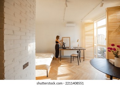 Interior Of Sunny Studio Apartment In Beige Tones With Working Place And Woman Spending Leisure Time At Home