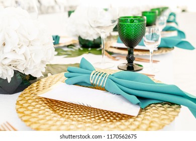 Interior of tent for wedding diner, ready for guests. Served round banquet table outdoor in marquee decorated hydrangea flowers, Golden dishes and green napkins. Catering concept