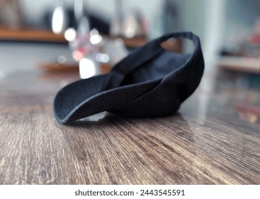 Interior top view visual image photo of a black cap hat upside down on a wood table in a house in close up with nobody around but during the bright day light