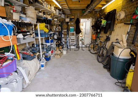 Interior of typical UK garage full of shelves tools, bikes, paint and ladders.
