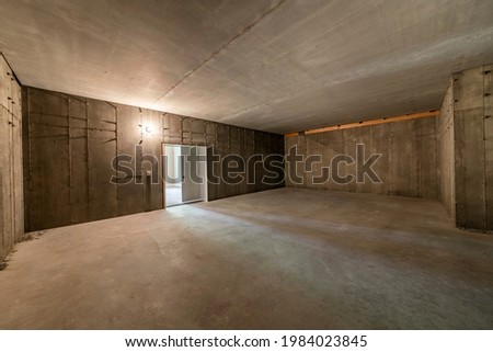 Interior of an under construction cold storage at the basement. Empty food storage room with concrete walls and floors, and a white door entrance to the white wall room.