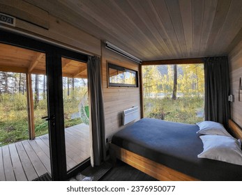 Interior of vacation rental forest lodge countryside cabin with large terrace and big window among trees for holidays in the wilderness. Modern hideaway cottage in wild pine forest on river bank.