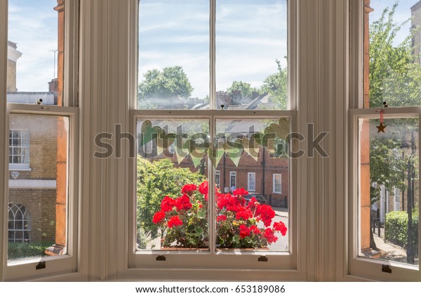 Interior of a Victorian British house with old\
wooden white windows  and red geraniums on the window sill facing a\
traditional English\
street
