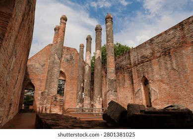 Interior view of the ancient assembly hall ruins at Wat Kudi Dao in Ayutthaya, Thailand. Tall weathered pillars stand among red brick walls and fallen debris under a beautiful bright cloudy blue sky