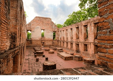 Interior view of the ancient assembly hall ruins at Wat Kudi Dao in Ayutthaya, Thailand. Red brick walls with rows of windows surround column bases on a tiled floor beneath a cloudy summer sky