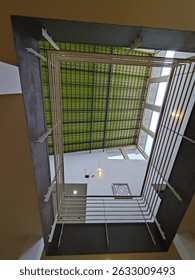 Interior view of a building, showcasing a high open-plan design.  The ceiling is composed of light-green tiles, and the architecture includes metal railings, creating an open, airy atmosphere. 