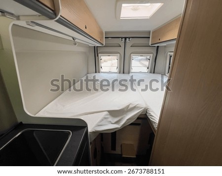 Interior view of a camper van featuring a comfortable double bed, cabinets, and a skylight, ready for a relaxing travel experience in Sabadell, Catalonia