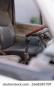 Interior view of a car featuring a gray leather driver's seat, wooden-finish steering wheel, and manual gear shift, highlighting vintage automotive design.